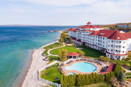 Aerial view of a coastal resort with a pool, beach, and landscaped grounds by the water.