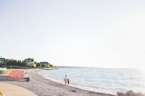 A serene beach scene with a person walking along the shore, colorful beach chairs, and a calm sea under a clear sky.