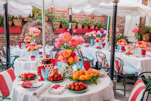 A vibrant outdoor dining setup with floral centerpieces, colorful tableware, and fresh fruit on tables surrounded by greenery.