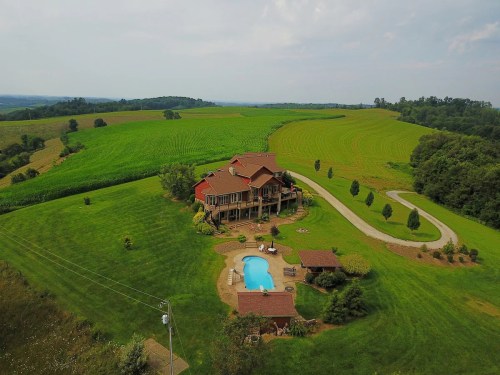 Aerial view of a large house with a pool, surrounded by lush green fields and rolling hills.