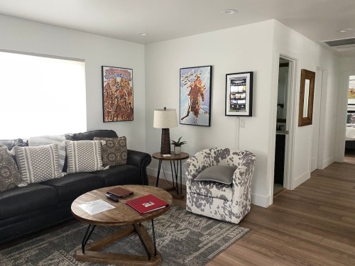 A cozy living room with a black sofa, patterned pillows, a wooden coffee table, and colorful wall art.