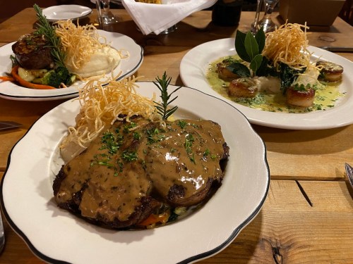 A table setting with two gourmet dishes: a steak with gravy and mashed potatoes, and scallops in a creamy sauce.