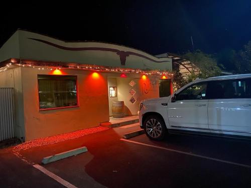 A dimly lit building with orange lights, a decorative bull horn, and a white SUV parked outside at night.