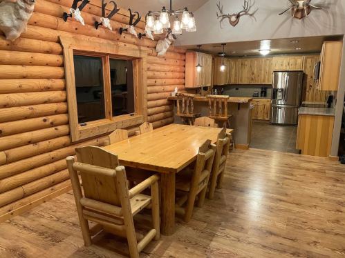 Cozy log cabin interior featuring a wooden dining table, chairs, and rustic decor with antlers on the walls.
