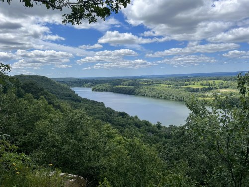 A scenic view of a river winding through lush green hills under a partly cloudy sky.
