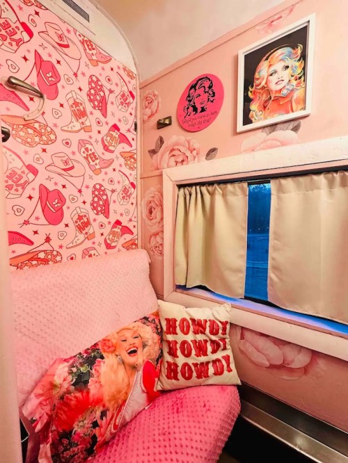 Cozy pink room with patterned walls, a plush sofa, decorative pillows, and vibrant artwork.