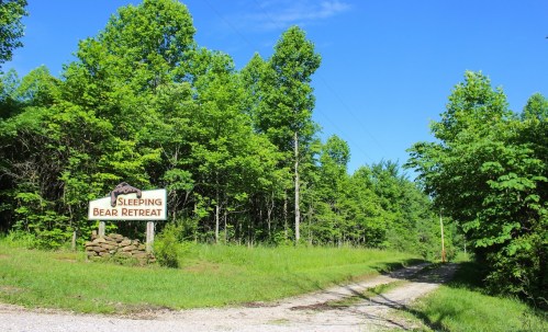 A sign for "Sleeping Bear Retreat" at the entrance of a green, wooded path on a sunny day.