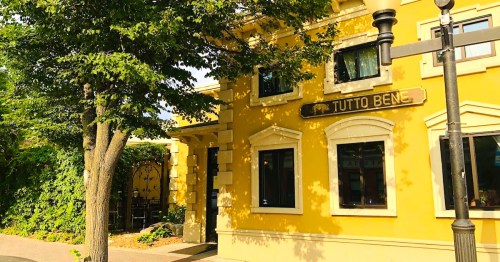 A yellow building with the sign "TUTTO BEN," surrounded by trees and greenery.