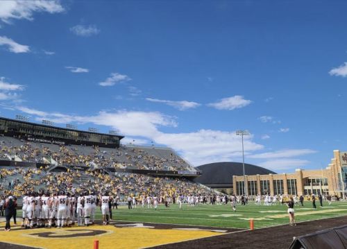 A football field with players and spectators under a clear blue sky at a stadium.