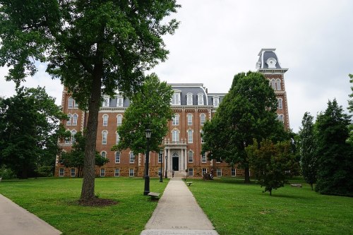 Historic brick building surrounded by trees and a grassy area, with a pathway leading to the entrance.