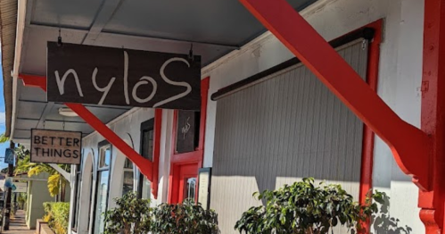 A storefront with a sign reading "nylos" and another sign saying "BETTER THINGS," featuring red accents and greenery.