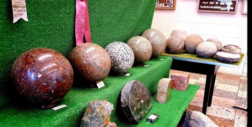 A display of polished stone spheres and rocks on green felt, showcasing various colors and textures.