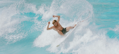 A surfer rides a wave, performing a maneuver with splashes of water around him in a vibrant blue ocean.