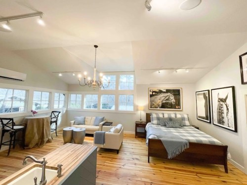 Cozy, modern studio with a bed, seating area, and large windows, featuring wooden floors and stylish decor.