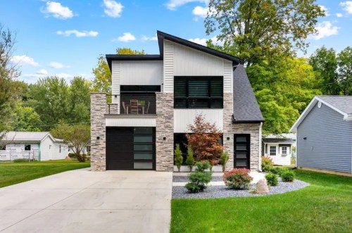 Modern two-story house with stone accents, large windows, and a landscaped yard on a sunny day.