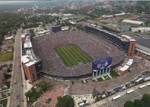 Aerial view of a packed stadium during a soccer match, with fans filling the stands and surrounding areas.