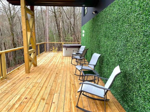 A wooden deck with four chairs and a green wall, surrounded by trees in a serene outdoor setting.