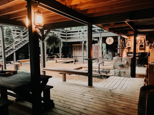 Cozy wooden interior with rustic decor, featuring tables, lanterns, and a staircase leading to an outdoor area.