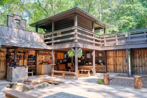 A rustic wooden cabin with multiple levels, surrounded by trees and featuring a spacious outdoor area.