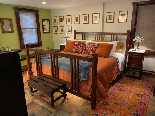 Cozy bedroom featuring a wooden bed, colorful pillows, lamps, and framed artwork on the walls. Warm, inviting decor.