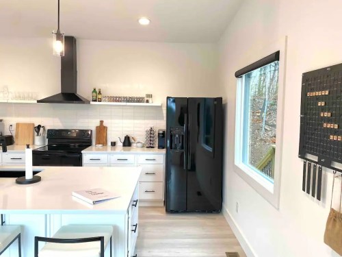 Modern kitchen with white cabinets, black appliances, and a large window overlooking a wooded area.