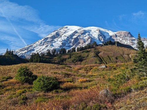 A snow-capped mountain rises above colorful autumn foliage under a clear blue sky.
