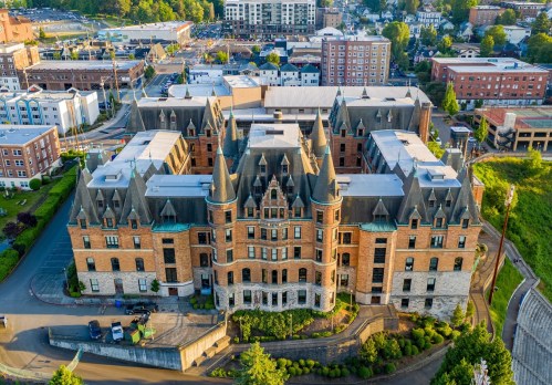 Aerial view of a historic brick building with turrets, surrounded by modern buildings and greenery.