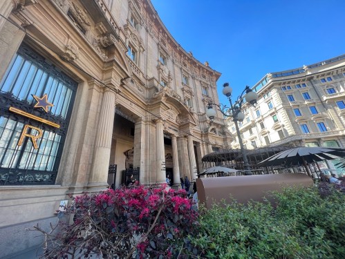 A grand building with ornate architecture, featuring a star sign and vibrant flowers in the foreground under a clear blue sky.