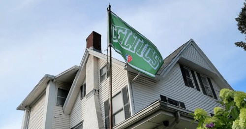 A white house with a green Celtics flag flying from a pole against a blue sky.