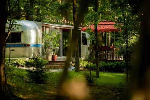 A vintage Airstream trailer surrounded by trees, featuring a cozy outdoor seating area with string lights.