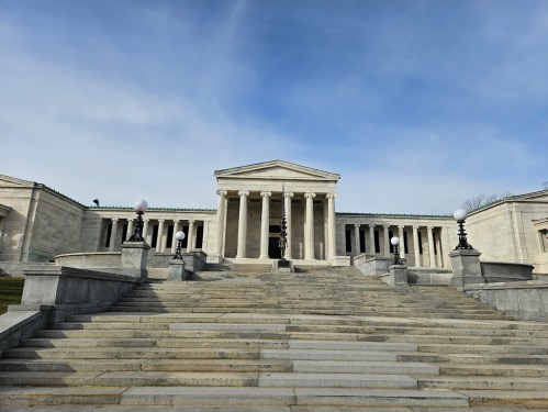 A grand stone building with columns, steps, and decorative lamps under a blue sky.