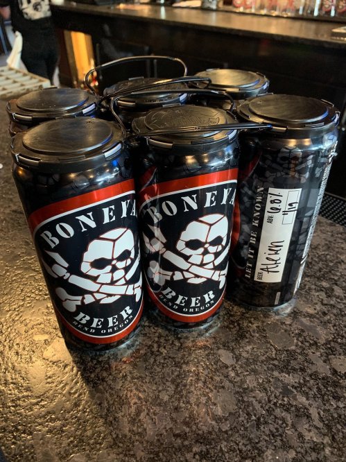Six cans of Bone Yard Beer with a skull logo, sitting on a bar counter. One can is labeled "Hazy IPA."