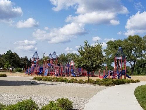 Colorful playground equipment with slides and climbing structures, surrounded by trees and a blue sky with clouds.