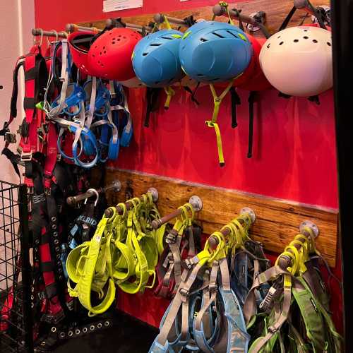 A wall display featuring various helmets and harnesses in bright colors, organized on hooks against a red background.