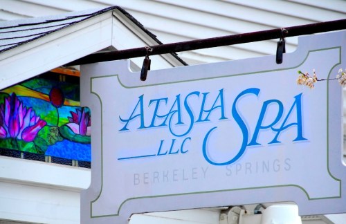 Sign for Atasia Spa, LLC in Berkeley Springs, featuring a colorful stained glass window with floral designs.