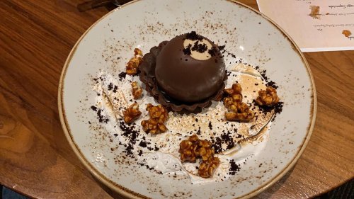A chocolate dessert on a plate, surrounded by popcorn and crumbs, with a creamy filling visible in the center.