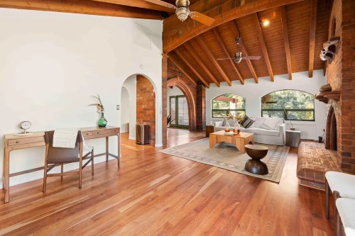 Spacious living room with wooden beams, a cozy sofa, and a coffee table, featuring large windows and warm wood floors.