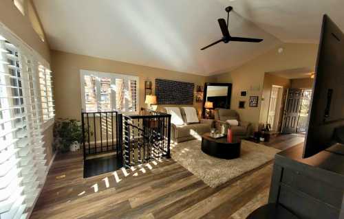 Bright living room with a ceiling fan, two sofas, a coffee table, and large windows, featuring wooden flooring and decor.