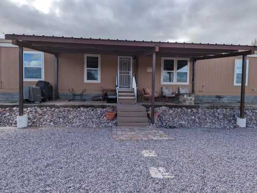 A mobile home with a covered porch, steps leading up, and gravel landscaping in front. Cloudy sky above.