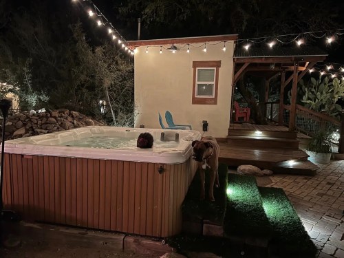 A hot tub with a person inside, a dog nearby, and a cozy outdoor setting with string lights and a wooden deck.