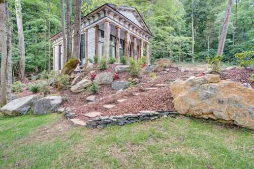 A small, classical-style building surrounded by trees, rocks, and landscaped gardens.