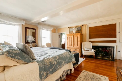 Cozy bedroom with a large bed, wooden furniture, and a fireplace, featuring natural light from windows.
