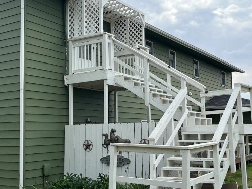 A white wooden staircase leads to a green building, with a lattice design and a white fence in the foreground.