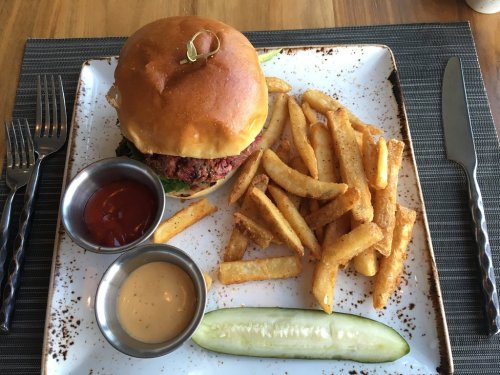 A plate with a burger, fries, a pickle, and two dipping sauces on a textured table setting.