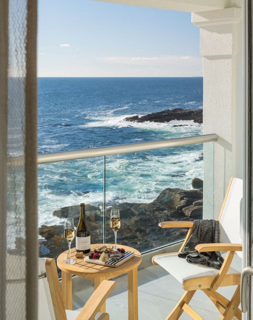 A balcony with a table set for two, featuring champagne and berries, overlooking a scenic ocean view.