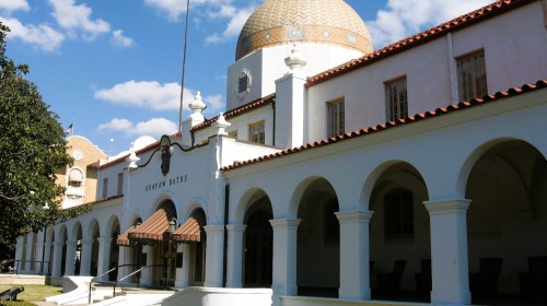 Historic building with a dome, arched windows, and a tiled roof, set against a blue sky with scattered clouds.