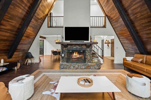 Cozy A-frame living room with a stone fireplace, modern furniture, and a large TV, featuring wooden accents and a warm atmosphere.