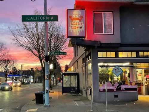 A colorful sunset behind a waffle shop with neon signage at the corner of California Ave and California St.