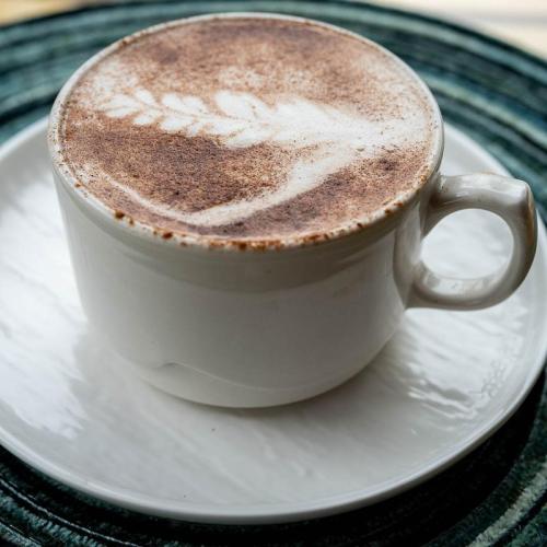 A cup of coffee with a decorative foam design, placed on a white saucer against a textured background.