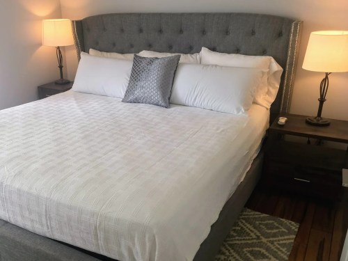 A neatly made bed with white linens and a decorative pillow, flanked by two lamps on nightstands.
